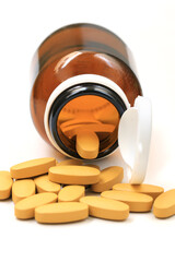 Pills of vitamin C spilled out open bottle on white background.