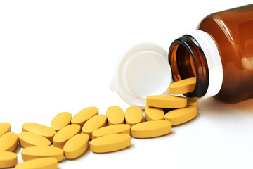 Pills of vitamin C spilled out open bottle on white background.