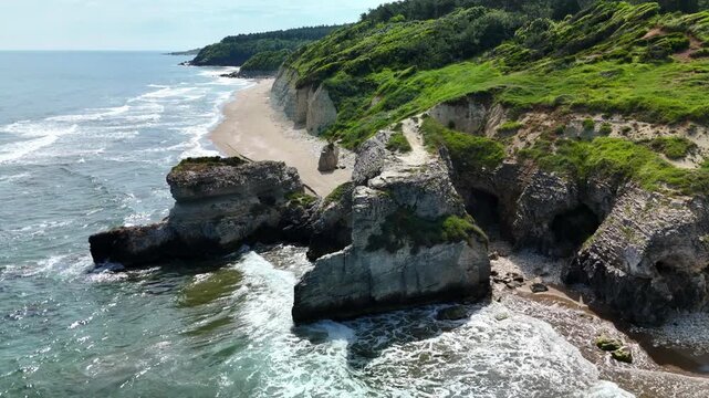 Aerial view of rocky coastline with waves crashing on a sunny day
