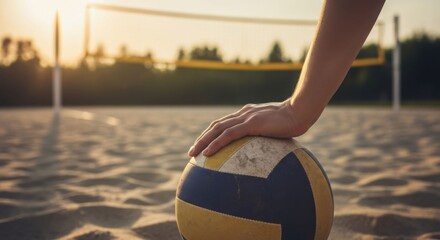 Close up of a man's hand on a volleyball on a sandy beach court with a net in the background. Healthy lifestyle.