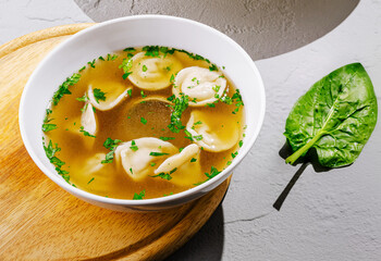 Warm dumpling soup served in a white bowl with herbs and spinach on wooden board