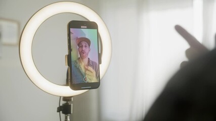 Content creator shooting video. Influencer filming on smartphone in ring light, with baseball cap, checkered shirt. Content for social media engagement and fans. Digital business streaming online - Powered by Adobe