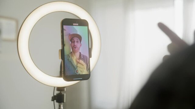 Content creator shooting video. Influencer filming on smartphone in ring light, with baseball cap, checkered shirt. Content for social media engagement and fans. Digital business streaming online