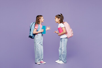 Full body little two friends children school girls 9-10 years old wear casual clothes backpack together hold books talk speak isolated on plain purple background Childhood education lifestyle concept
