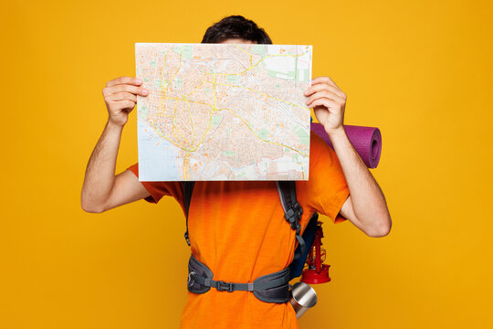 Young traveler man carry backpack with stuff mat reading paper map isolated on plain yellow background. Tourist leads active healthy lifestyle walk on spare time. Hiking trek rest travel trip concept.