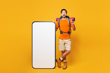 Young traveler man carry backpack with stuff mat big blank screen have idea isolated on plain yellow background. Tourist leads active lifestyle walk on spare time Hiking trek rest travel trip concept