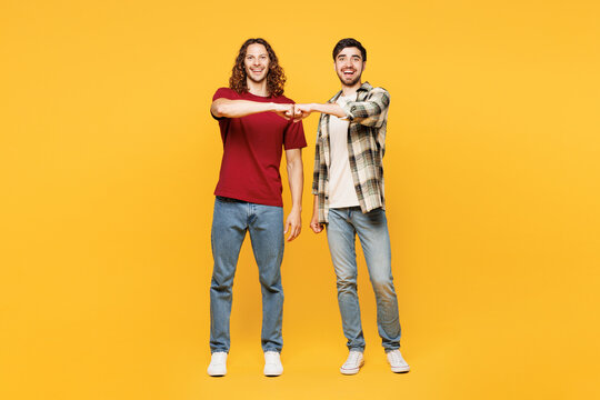 Full body young happy fun two friends buddies men they wear casual clothes together look camera do fist bump gesture isolated on plain yellow orange color background studio portrait Lifestyle concept