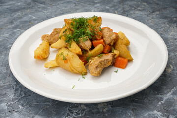 stewed potatoes with vegetables in a white plate on a gray background