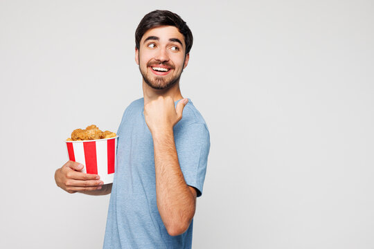 Young man wear blue t-shirt casual clothes hold takeaway box with barbecue chicken meat wings point finger aside isolated on plain solid white background. Proper nutrition healthy food choice concept.