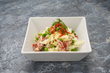 salad with cabbage, sausage and peas in a white plate on a gray concrete background