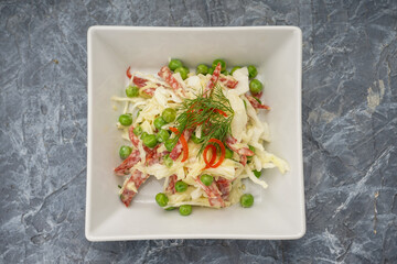 salad with cabbage, sausage and peas in a white plate on a gray background