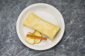 pancake with apple and cinnamon filling in a white plate on a gray background