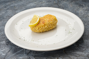 fish cutlet with lemon in a white plate on a gray concrete background