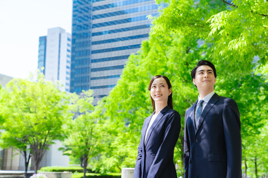 A group of male and female business people looking up at the sky in a city with fresh greenery