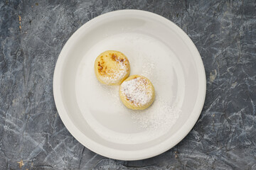 breakfast cheesecakes with powdered sugar in a white plate on a gray background