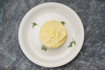 mashed potatoes with herbs in a white plate on a gray concrete background