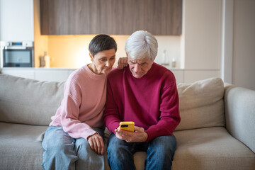 Worried puzzled senior husband and wife studying phone screen on sofa. Fraudulent message, online security risks, elderly vulnerability to scam, digital deception, financial fraud, cybercrime aware