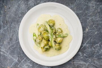 boiled brussels sprouts with cream sauce in a white plate on a gray background