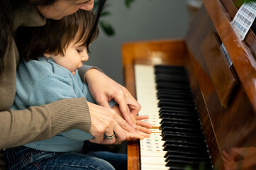 Child exploring music with loving guidance at a cozy piano during a sunny afternoon in a warm home setting, creating joyful memories through playful learning