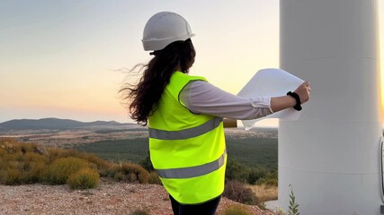 Female engineer inspecting wind turbine farm at sunset - Powered by Adobe