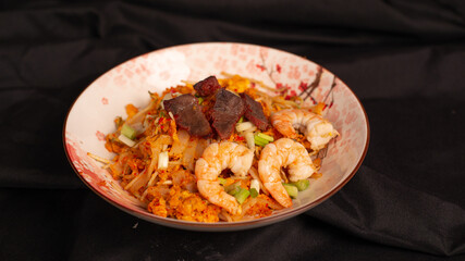 Stir fried kwetiau with shrimp and lapchiong. Served on brown stone plate. Isolated from black background. Perfect for recipe, article, catalogue, promotion, or any cooking contents
