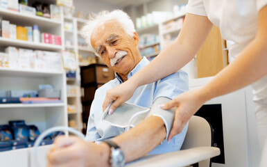 Fototapeta premium Female pharmacist checking an elderly man blood pressure in a pharmacy.