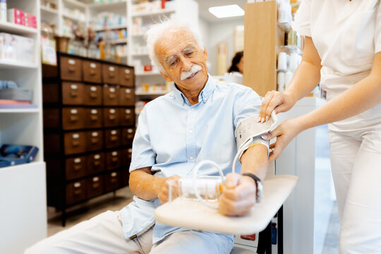 Female pharmacist checking an elderly man blood pressure in a pharmacy. - Powered by Adobe