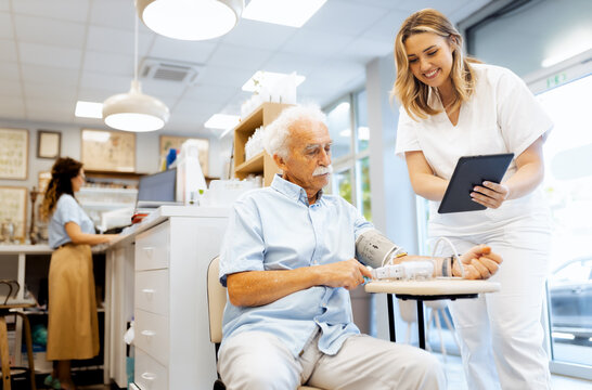 Female pharmacist checking an elderly man blood pressure in a pharmacy and consults him about the appropriate medication.