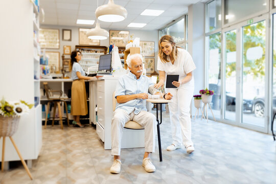 Female pharmacist checking an elderly man blood pressure in a pharmacy and consults him about the appropriate medication. - Powered by Adobe