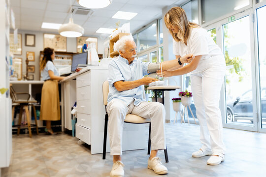Female pharmacist checking an elderly man blood pressure in a pharmacy.
