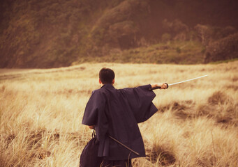 A samurai in black is running via meadow and forest nearby ocean in New Zealand.