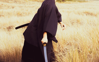 A samurai in black is running via meadow and forest nearby ocean in New Zealand.