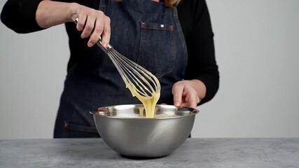 Close Up of Professional Cook Whisking Eggs in a Shiny Metal Bowl with a Whisk Against Light Grey Background Demonstrating Culinary Expertise in Food Preparation Techniques for Ads and Recipe
