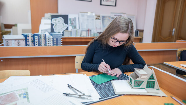 Caucasian young woman making a model of a building. Student of the construction university.