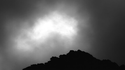 Dramatic mountain silhouette against a bright cloudy sky in black and white landscape showcasing