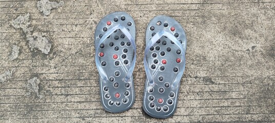A pair of gray reflexology massage slippers with black and red acupressure points, placed on a...