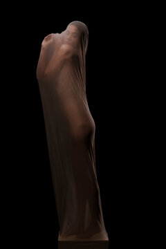 A woman is enveloped in a sheer, translucent fabric, revealing her body's contours against a dark background. Her eyes are closed, conveying a sense of introspection or calm.
