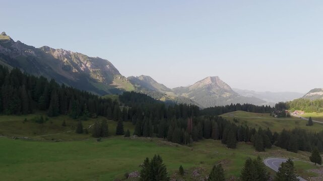 Forward aerial of Santis at dawn sweeps over Schwagalp meadows and dark fir forests, with a classic Swiss hut in frame and summer sky, showcasing an alpine valley.