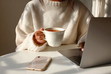 A woman working on a laptop while sipping hot tea phone casual cup.