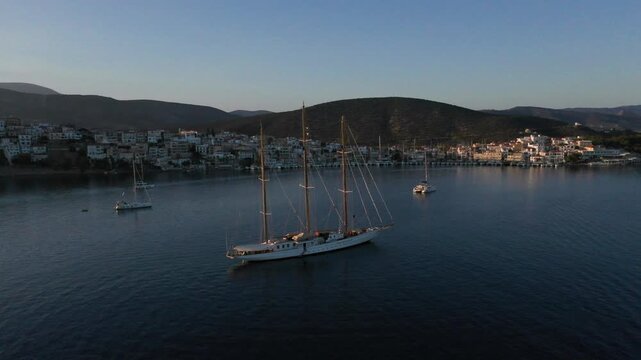 Ermioni, Greece - 29 July 2025: Aerial view of a majestic sailing boat gliding on the tranquil waters near Ermioni, contrasting with the distant town and hills.