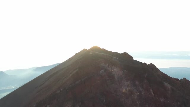 Aerial view of the majestic Mount Rinjani's peak with people silhouetted against a bright sky, the rugged terrain creates a stark contrast, Mount Rinjani, West Nusa Tenggara, Indonesia.