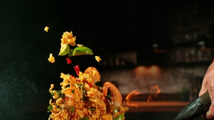 Super Slow Motion of Flying Spanish Paella Meal with Shrimps and Vegetable. Filmed on High Speed Cinema Camera, 1000 fps. Blur Kitchen Interior on Background, Flames Burning Around. Speed Ramp Effect. - Powered by Adobe