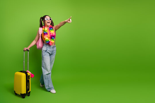 Happy young traveler pointing direction with luggage on bright green background emphasizing summer vacation vibes - Powered by Adobe