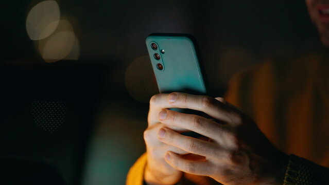 Freelancer hands typing sms at cellphone in dark apartment closeup. Man tapping