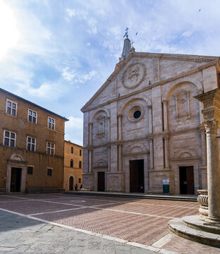 Pienza, Tuscany, Italy - 23 April 2025: View of the Piazza Pio II, a symphony of travertine and brick under a vast sky, where the Duomo's facade catches the sun's golden kiss.