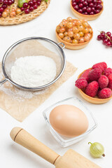 Flour in sieve, egg in small glass bowl. Tartlets with berries