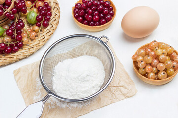 Flour in sieve, egg. Tartlets with berries.