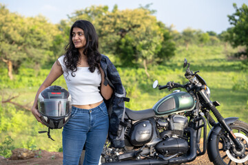 Strong independent Indian woman biker: beautiful girl, stylish rider, motorcycle adventure, elegant jacket, confident posture, powerful machine, free spirit, road journey, fearless attitude.