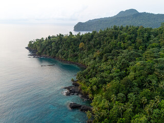 Aerial view of São Tomé’s tropical coastline near São João dos Angolares, with turquoise waters, black volcanic rocks, and dense palm forest.