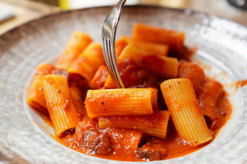 Closeup of a young traveler eating Rome's famous pasta, Rigatoni Amatriciana ( Rigatoni all’ Amatriciana)